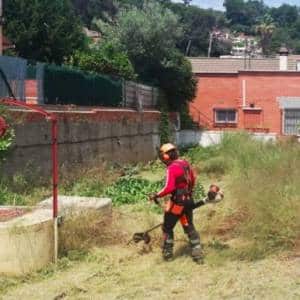 Operario con desbrozadora manual limpiando el matorral de un jardín