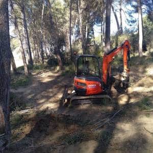 Mini excavadora desbrozando los márgenes de un camino forestal